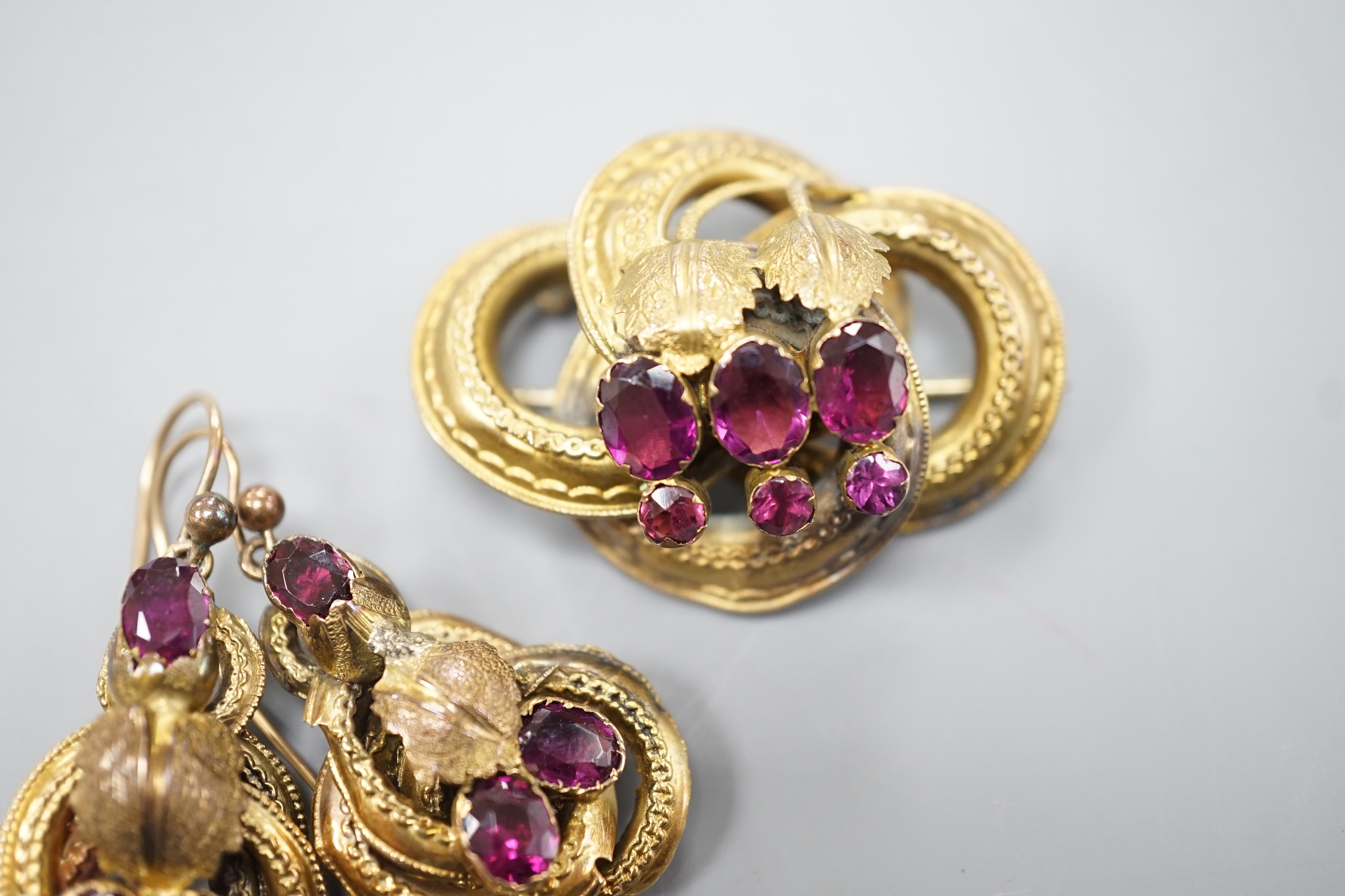 A Victorian yellow metal, oval and round cut garnet set demi parure, comprising a scroll work brooch and pair of matching earrings(a.f.), brooch, 38mm, gross weight 14 grams.